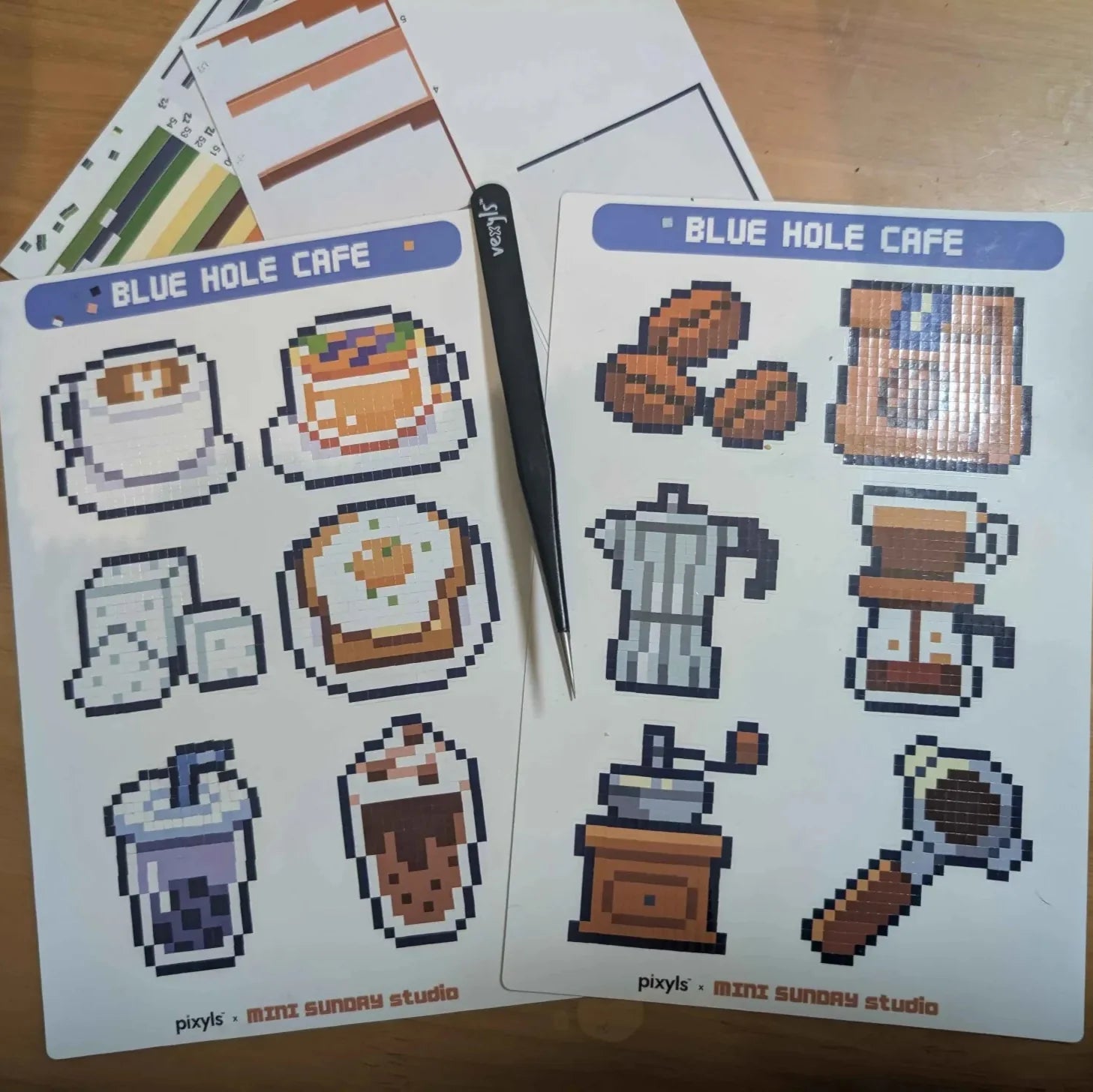 Sticker sheet with pixel art designs of coffee-themed items from Blue Hole Cafe on a wooden surface.